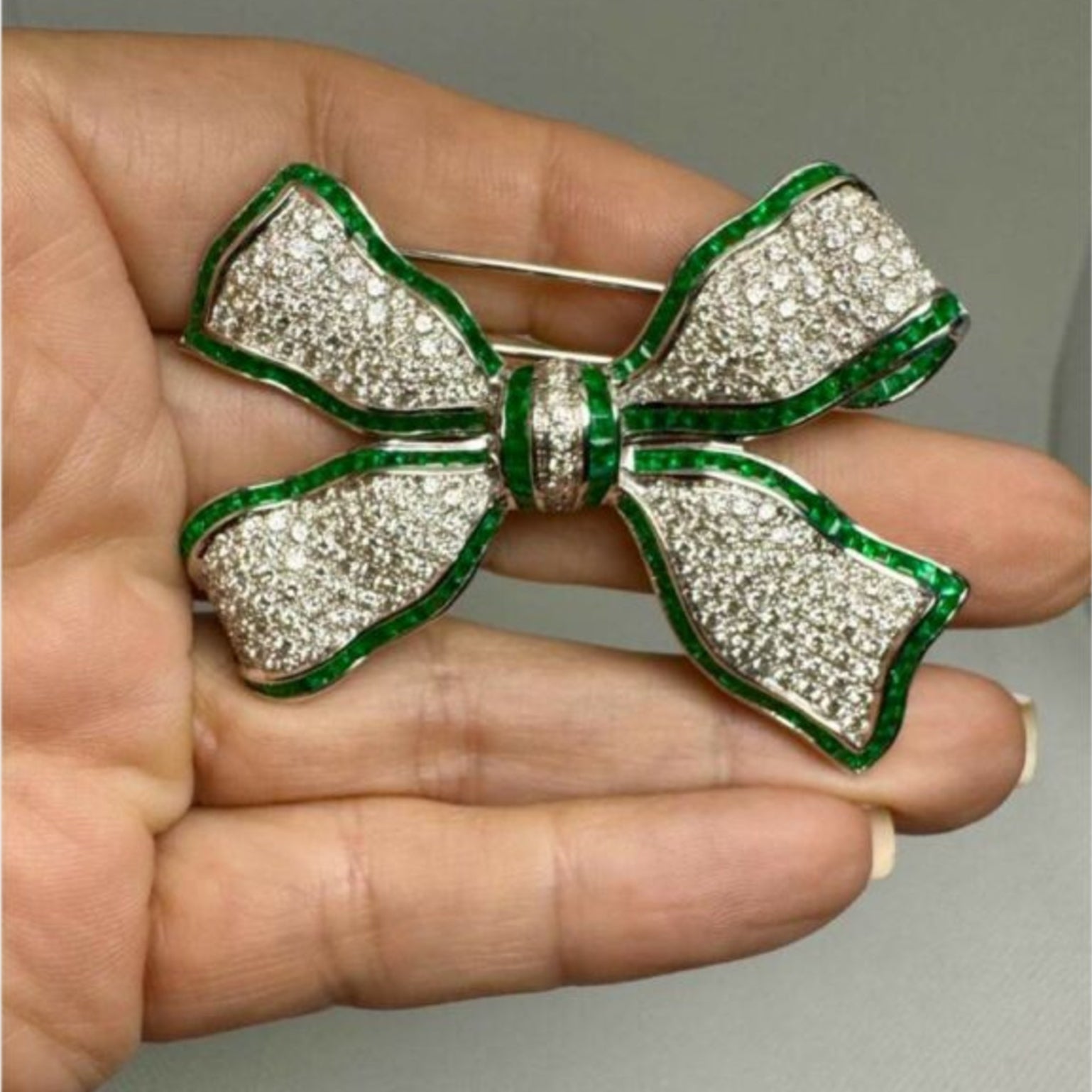 Post-1980s Platinum Diamond & Emerald Bow Brooch in hand