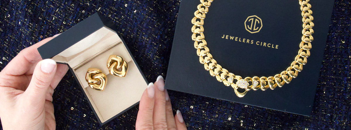 Gold chain necklace on a 'Jewelers Circle' card with a hand holding a box of gold earrings.