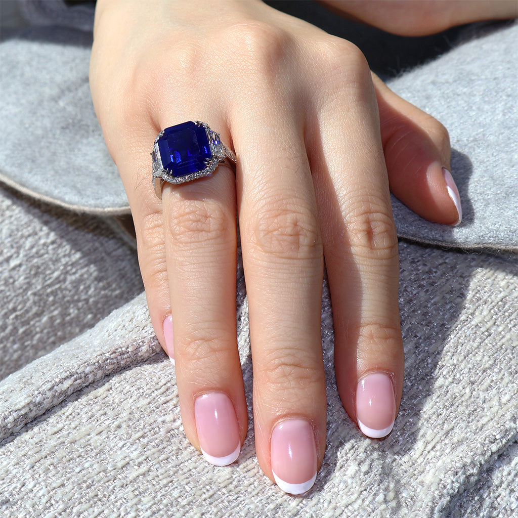 Hand wearing a ring with a blue gemstone on a textured surface